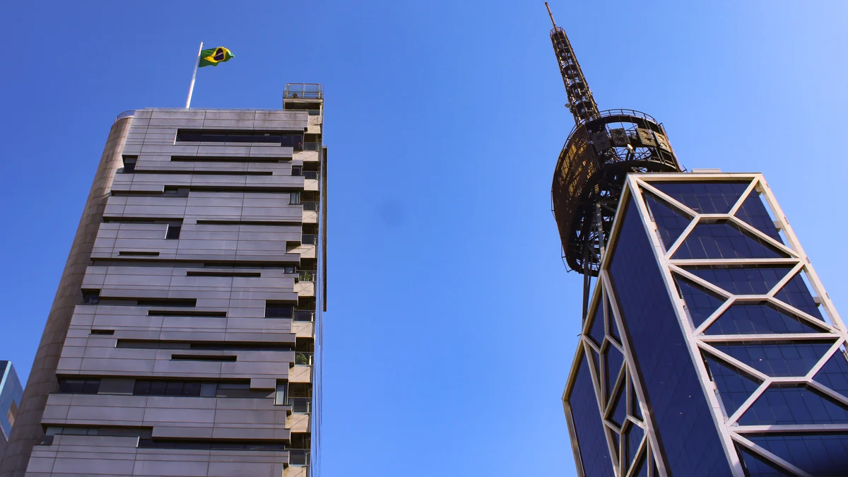 Dos edificios altos vistos desde abajo contra el cielo azul, uno con estructura exterior diagonal