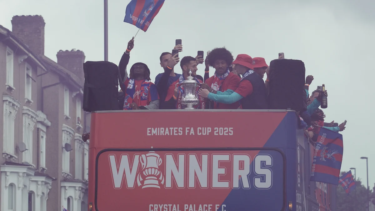 Jugadores del Crystal Palace celebran con un trofeo sobre un autobús rojo y azul