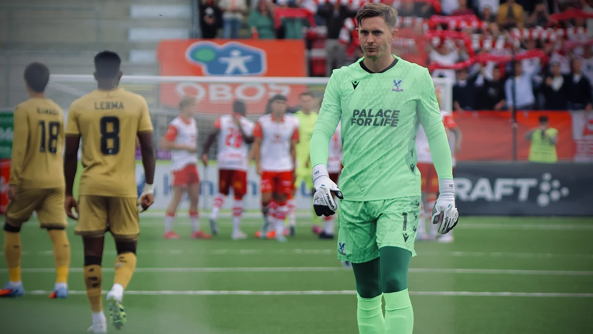Portero del Crystal Palace con uniforme verde camina por el campo con jugadores al fondo