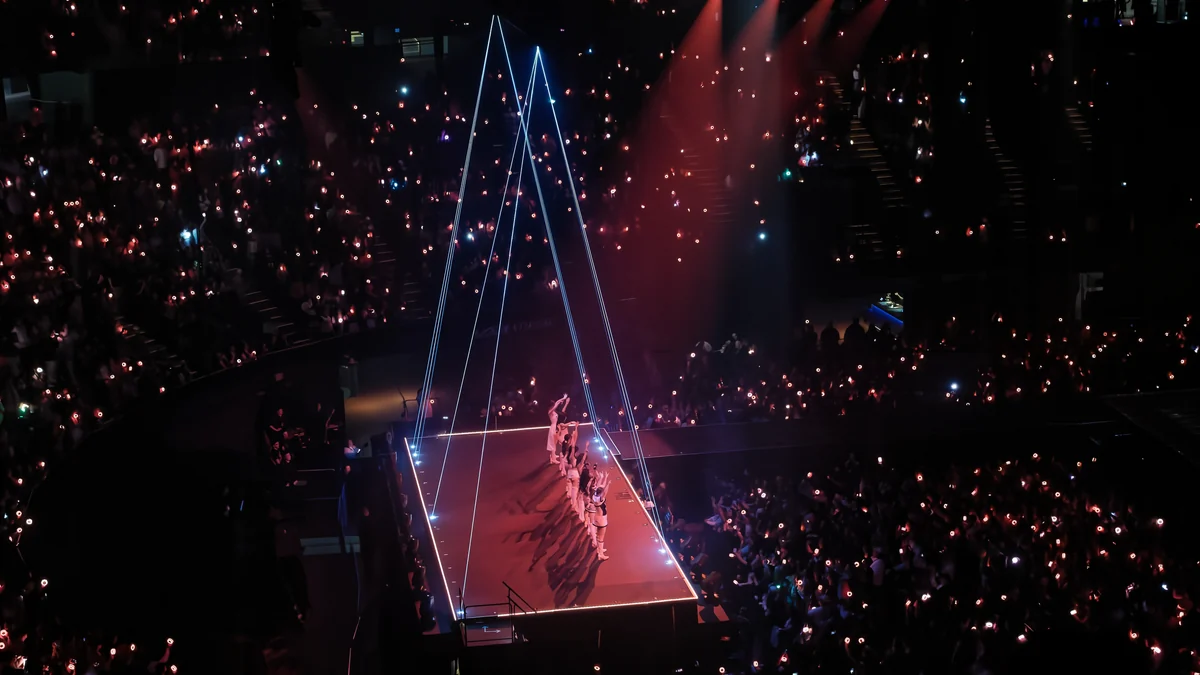 TWICE actúa sobre una pasarela rodeada por el público y puntos de luz en una arena.