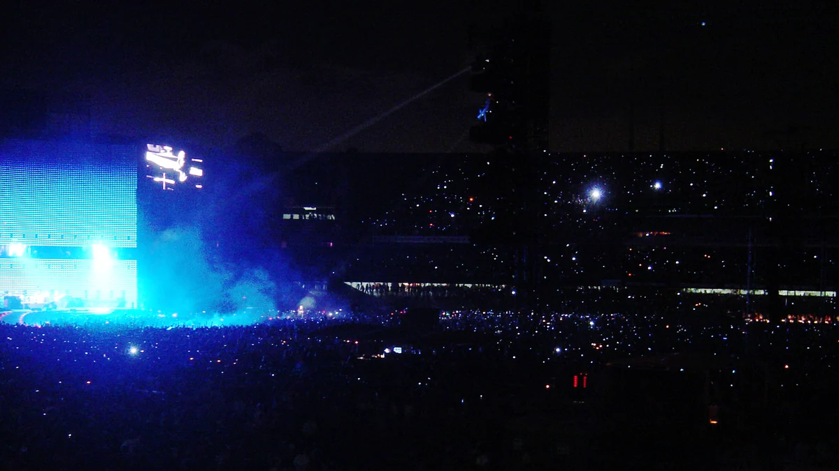 Stade sombre et rempli pendant un concert de U2, avec scène bleue à gauche et lumières du public