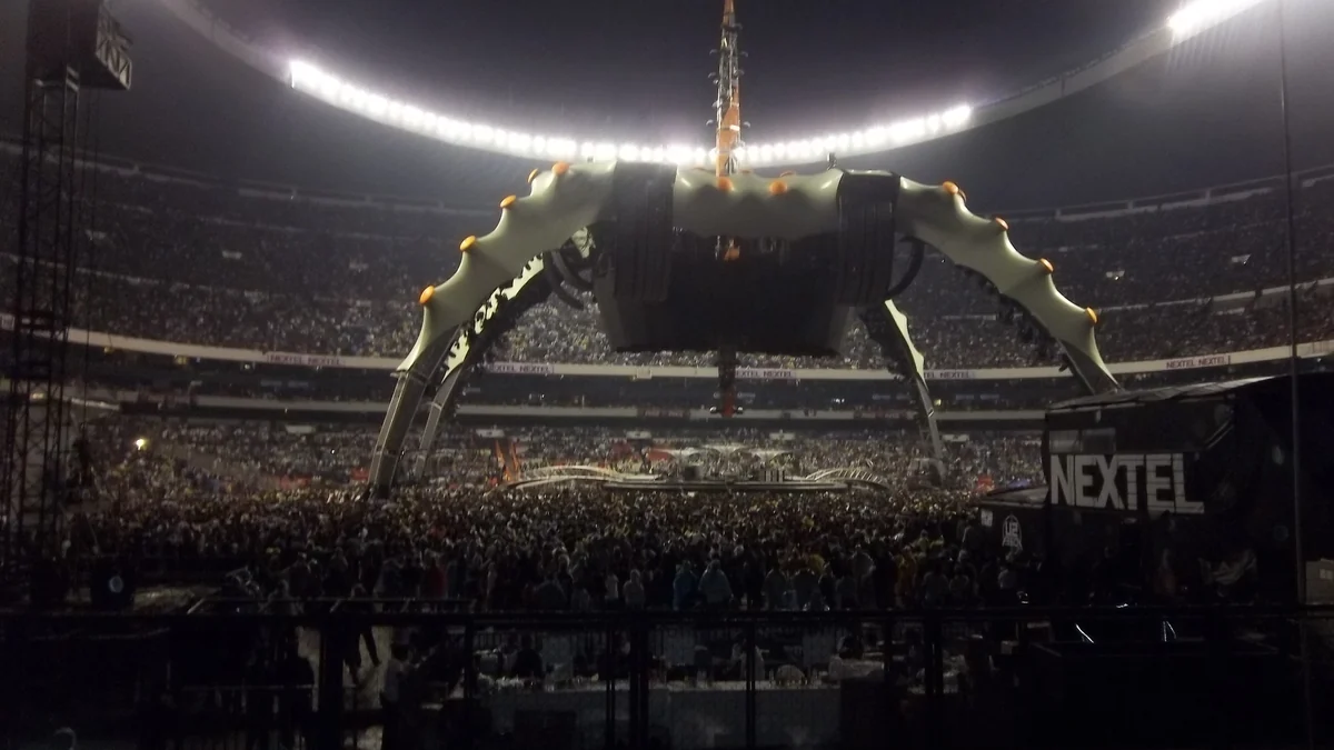 Stade rempli face à une grande structure scénique à quatre arches lors d’un concert de U2