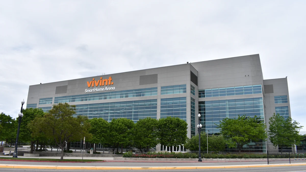 Glass-fronted facade of Vivint SmartHome Arena, with trees and a street in the foreground.