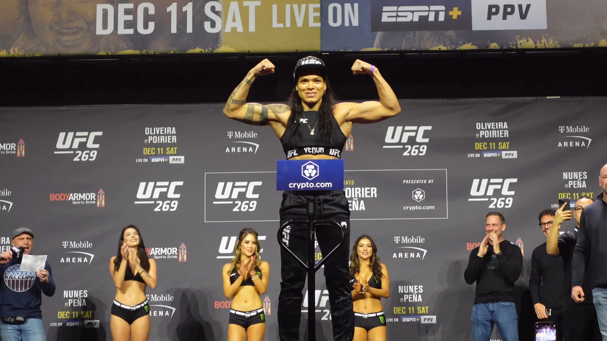 Amanda Nunes sonrí y flexiona los brazos sobre la báscula en el escenario del pesaje de UFC 269.