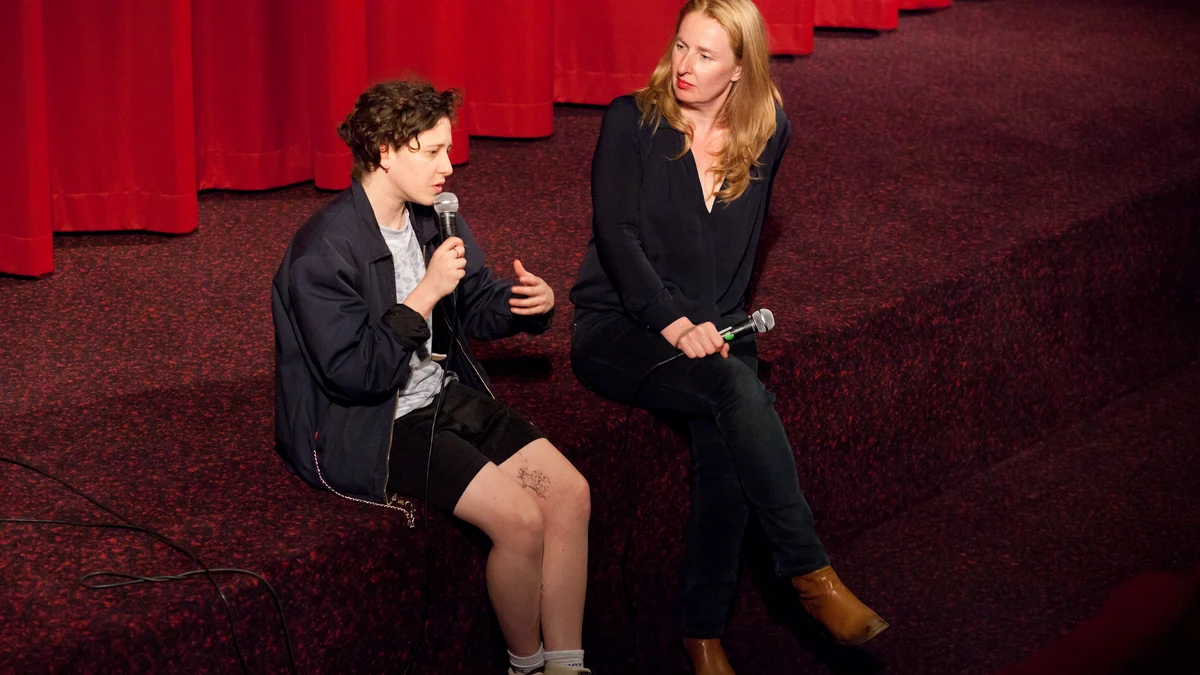 Mica Levi fala ao microfone ao lado da moderadora Petra Erdmann em uma sala de cinema