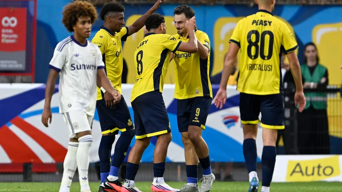 Jogadores do Union Saint-Gilloise de amarelo comemoram em campo ao lado de um adversário de branco.