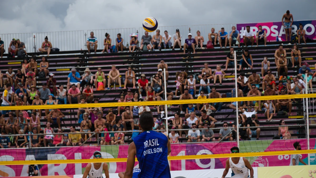 Brazilian player seen from behind at the net as the ball crosses in front of a crowded grandstand
