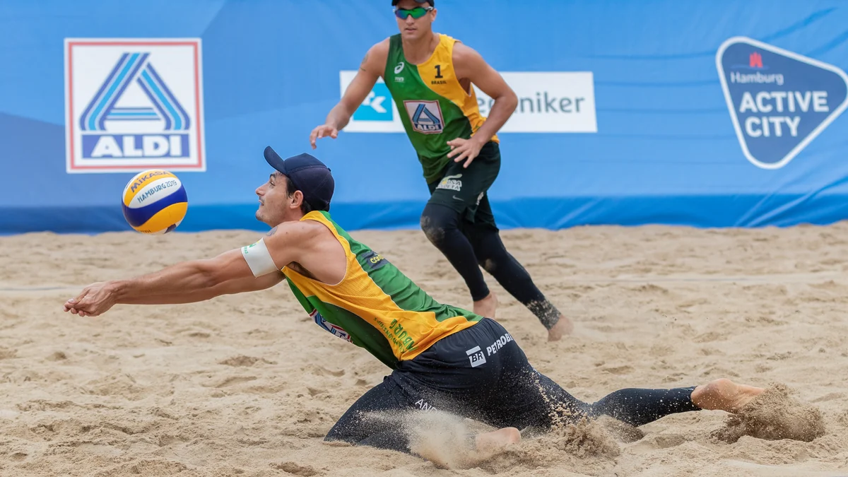 André Loyola Stein dives across the sand to receive the ball, with George Wanderley behind him