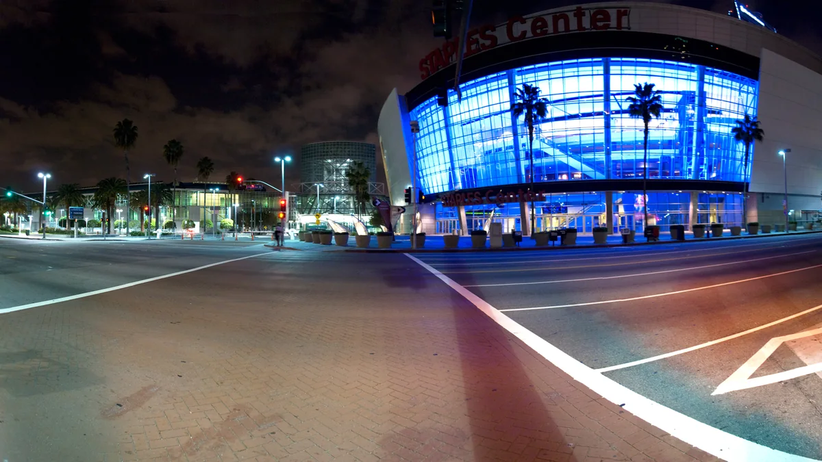 Exterior do então Staples Center iluminado em azul à noite, visto do outro lado de uma avenida vazia