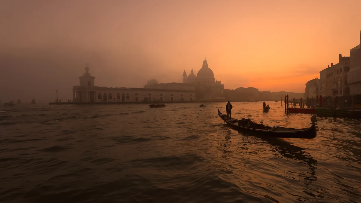 Gondole en silhouette sur l’eau de Venise sous un ciel orangé