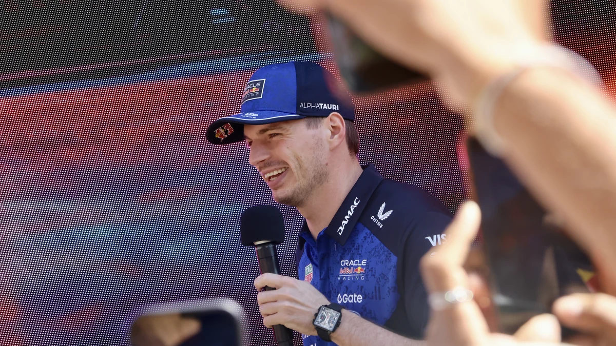 Max Verstappen, con gorra azul, habla por un micrófono ante una pantalla LED