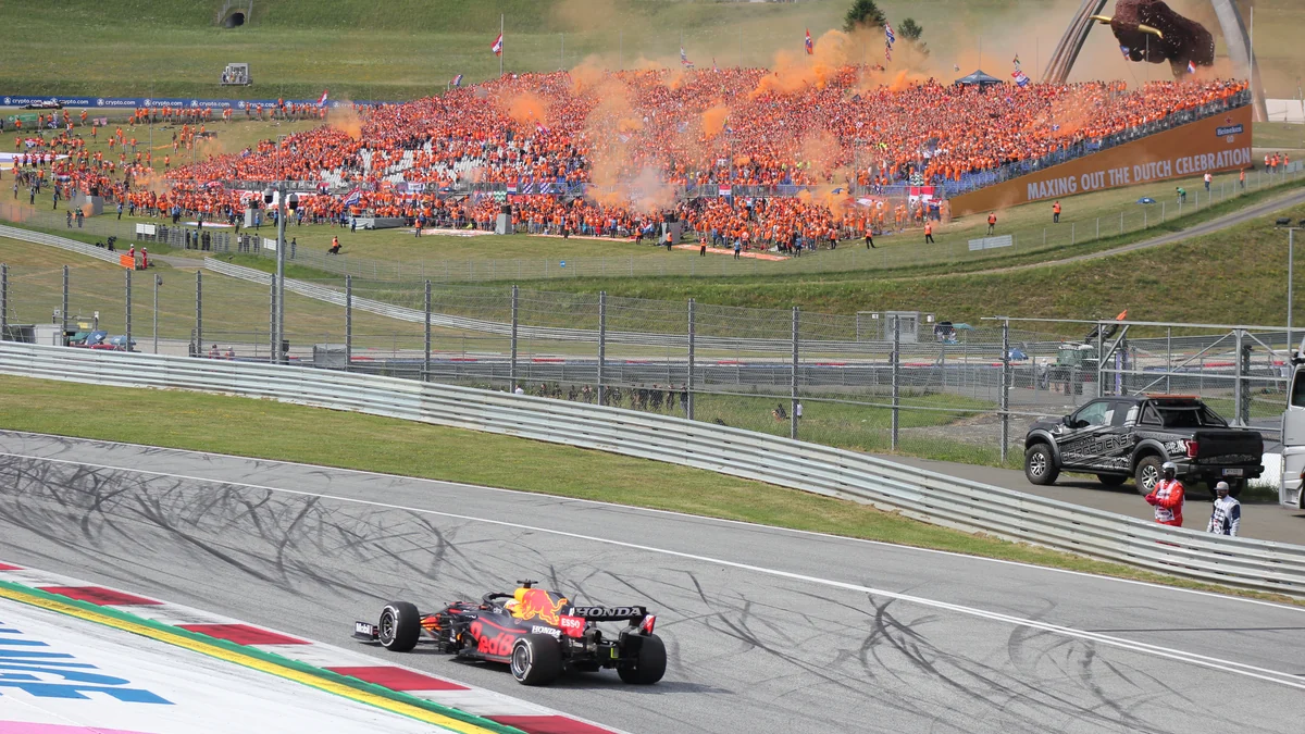 Monoplaza de Fórmula 1 de Red Bull en pista ante una grada llena de aficionados vestidos de naranja