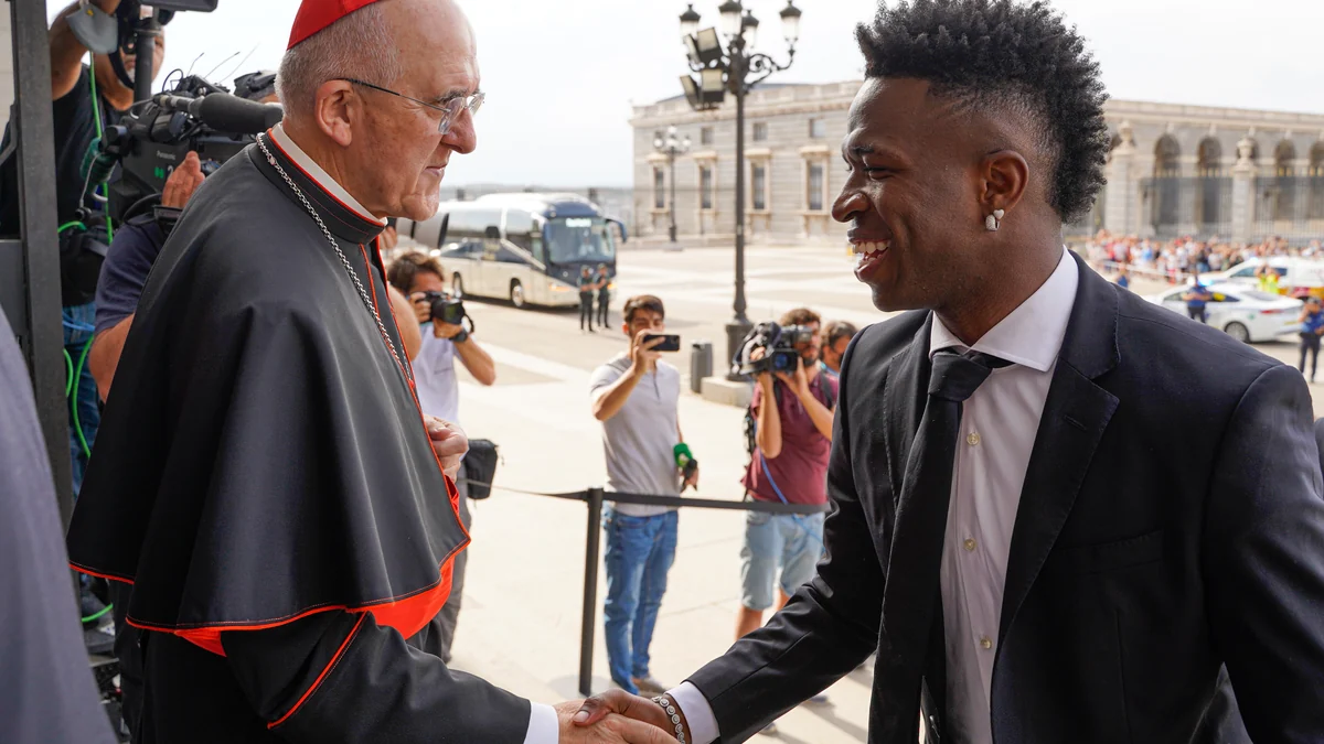 Vinícius Júnior, en costume noir, salue un membre du clergé devant des photographes.