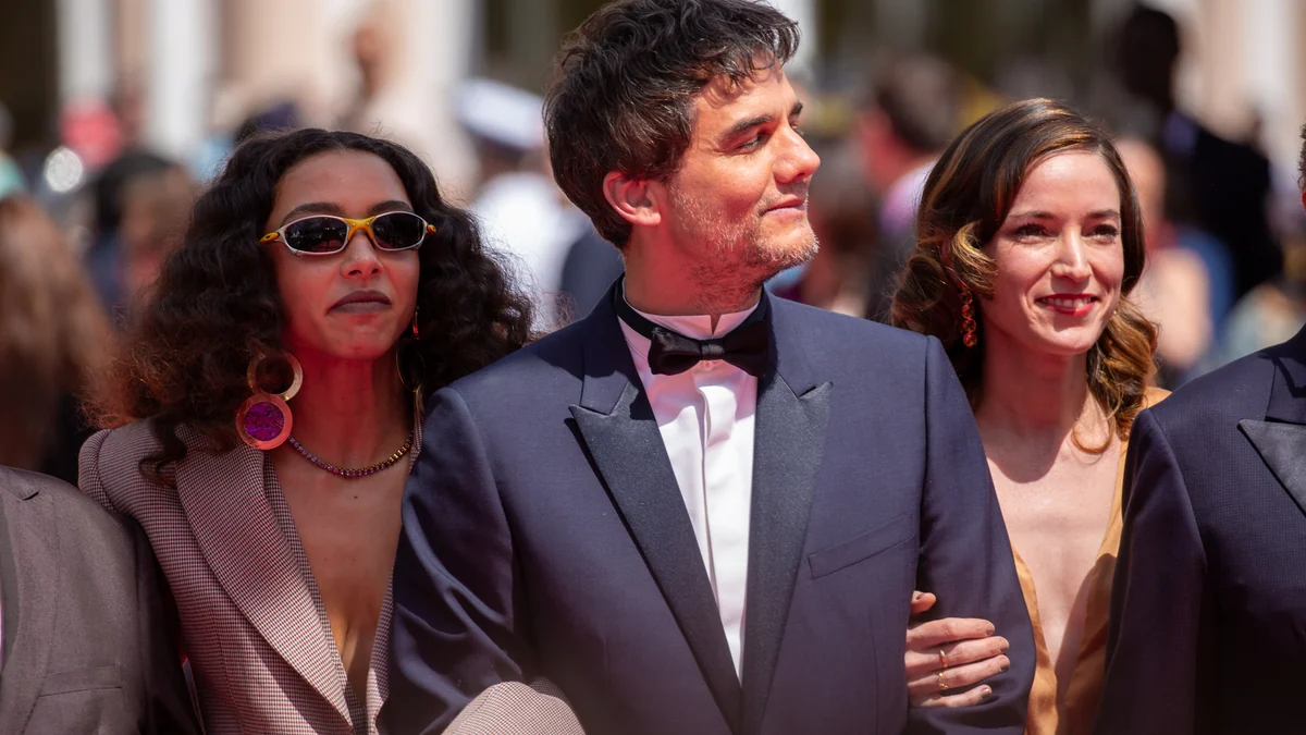 Alice Carvalho, Wagner Moura in a tuxedo and Emilie Lesclaux pose together on a red carpet