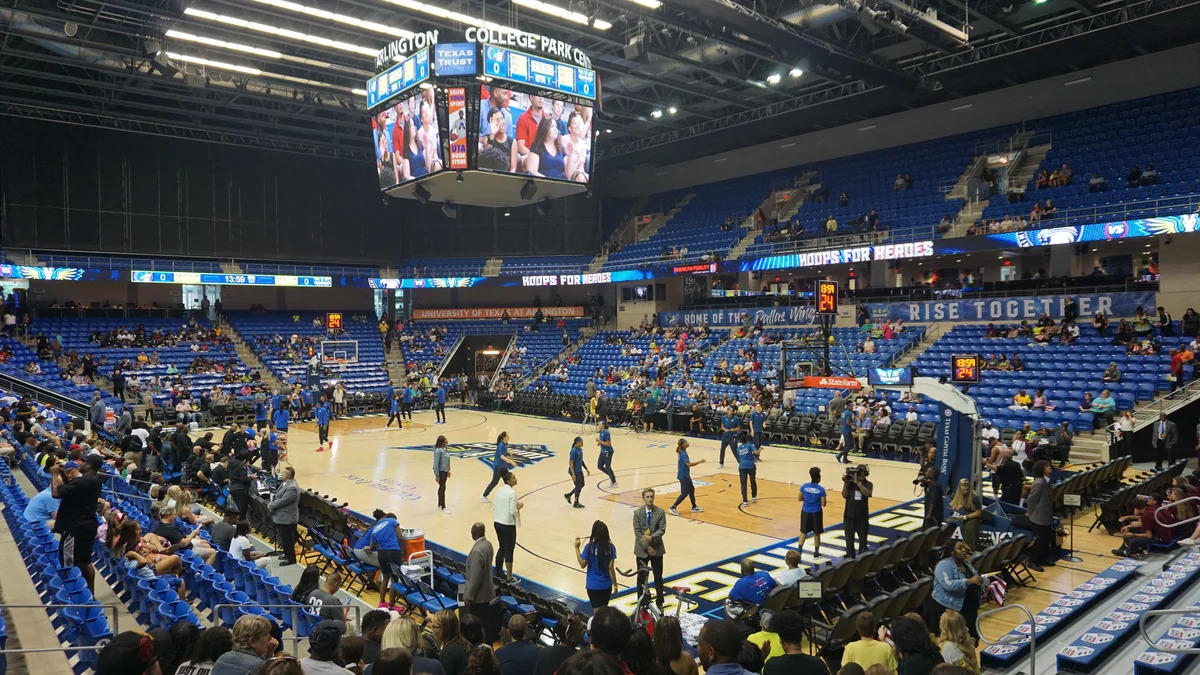 Vista ampla da quadra e das arquibancadas azuis durante o aquecimento em uma arena de basquete.