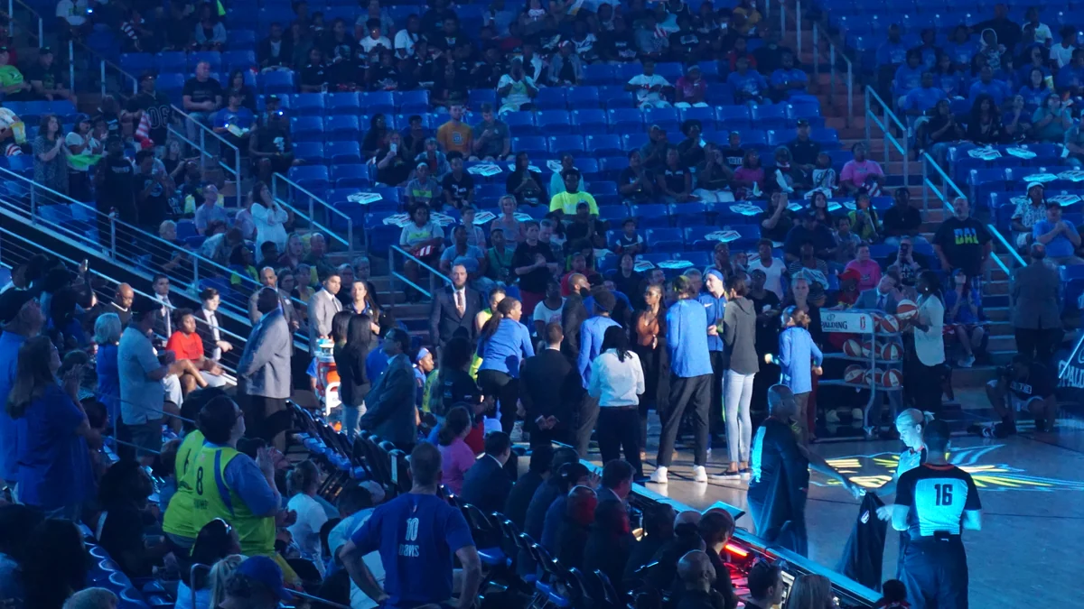 Integrantes de uma equipe de basquete reunidas na lateral da quadra sob iluminação azul.