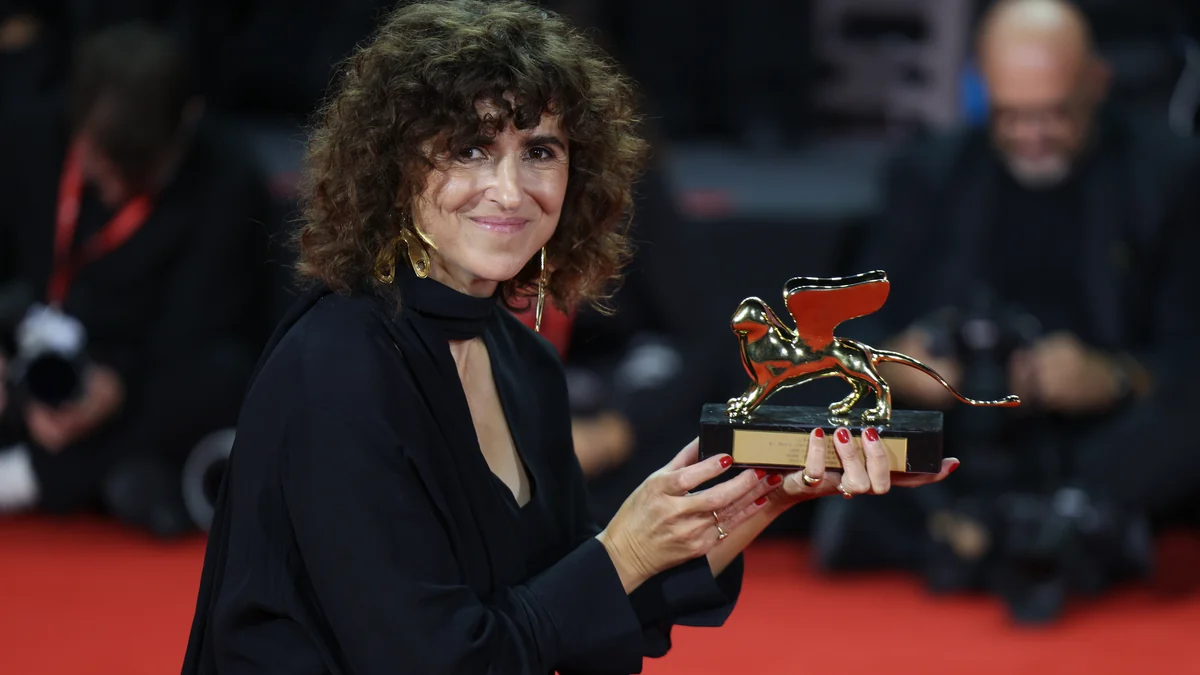 Woman dressed in black holds a golden lion-shaped trophy on a red carpet.