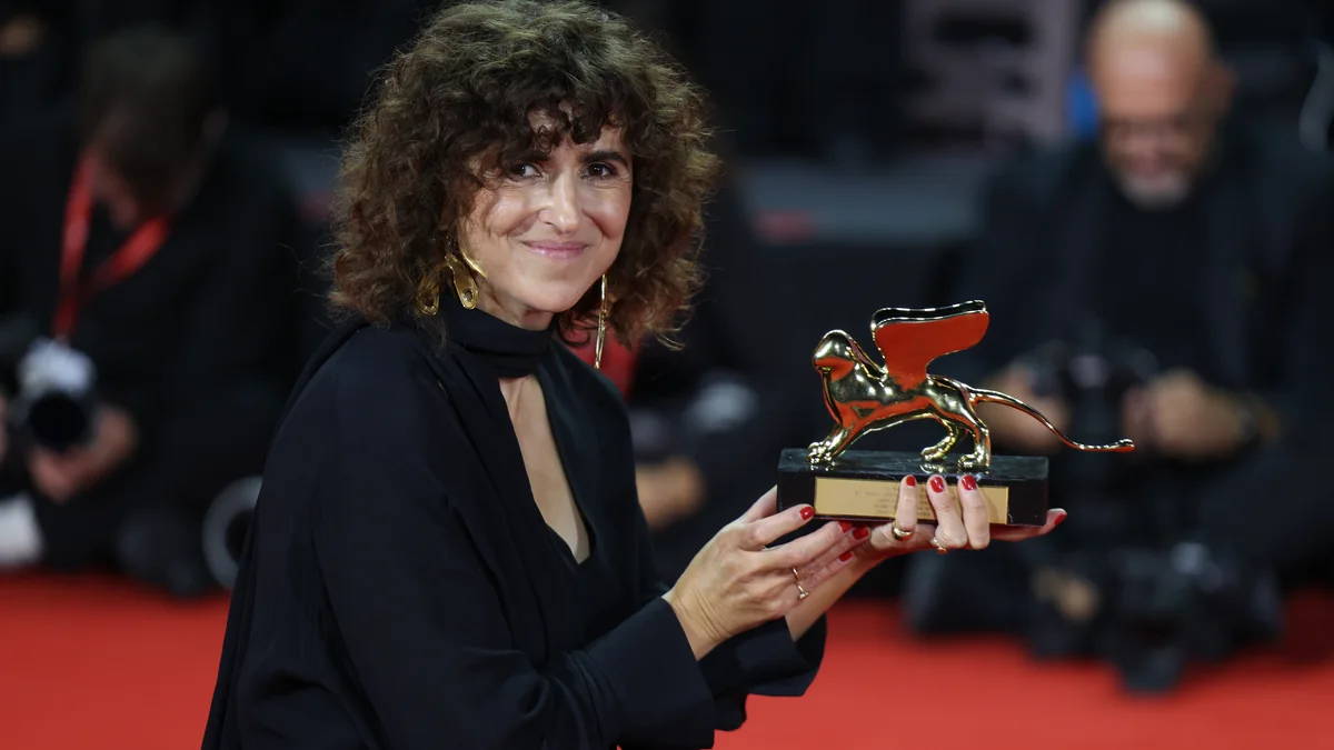 Mulher de preto segura o troféu dourado em forma de leão sobre um tapete vermelho.