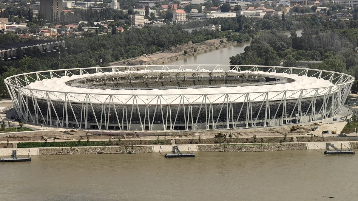 Aerial view of a large oval athletics stadium beside a river and surrounded by trees.