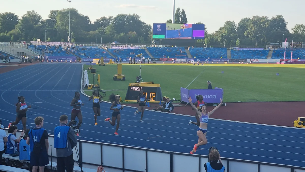 Sprinter wearing a Hunt bib crosses the finish with her arms raised ahead of other runners.