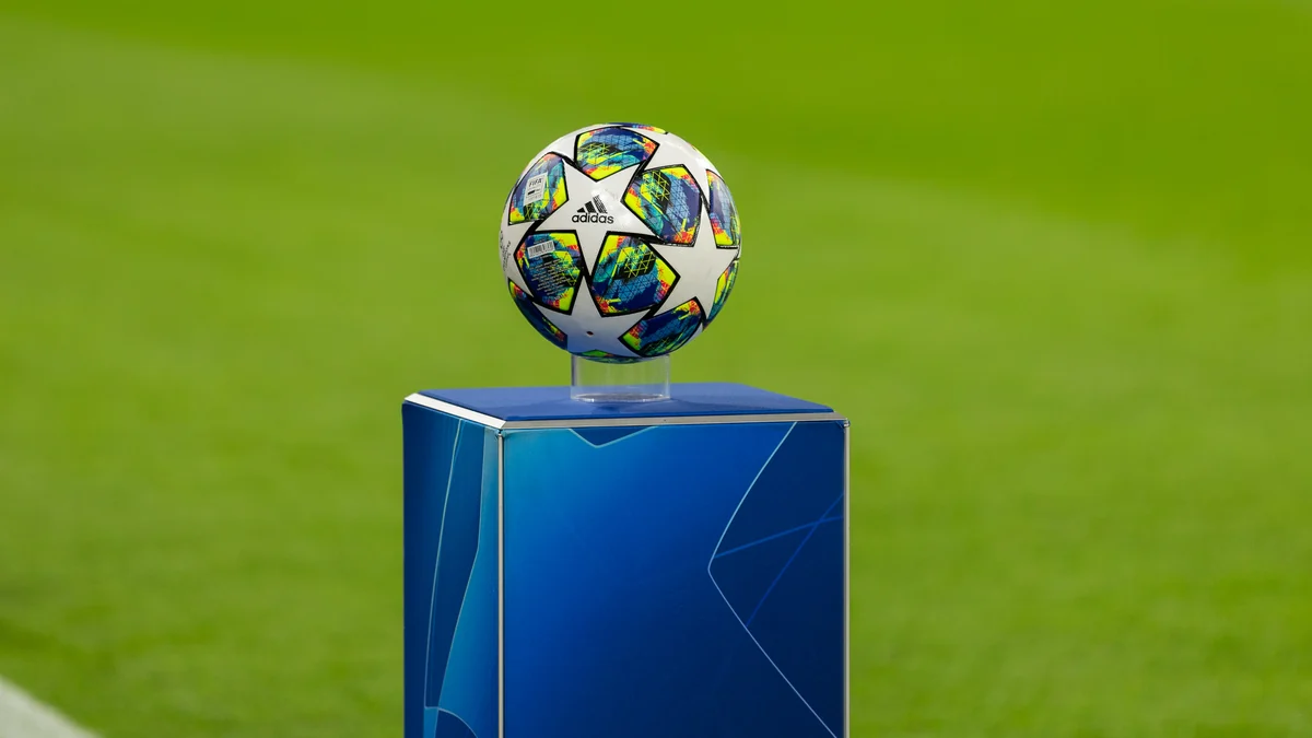 Bola da Champions League exposta sobre um pedestal azul à beira do gramado.