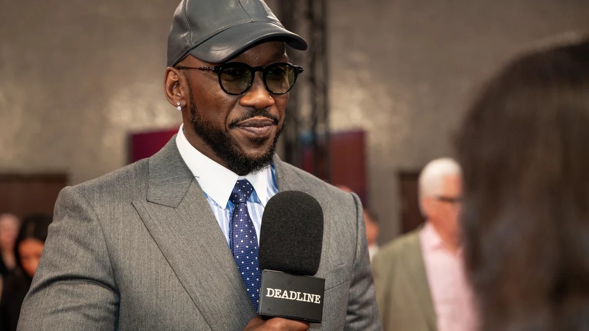 Mahershala Ali con traje gris, gorra y gafas durante una entrevista en un evento